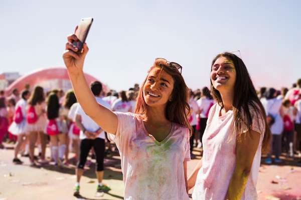 Portrait of a happy young women taking selfie on mobile phone during holi festival 