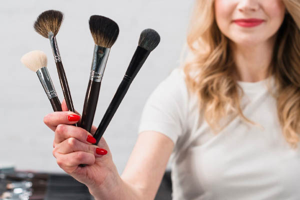 smiling-visagiste-woman-holding-cosmetic-brushes